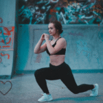A woman in athletic wear doing a lunge exercise in front of a graffiti wall.