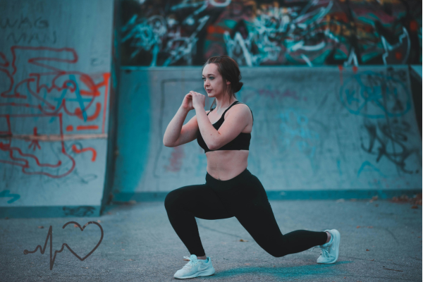 A woman in athletic wear doing a lunge exercise in front of a graffiti wall.