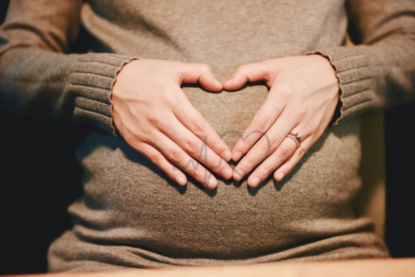 Close-up of a pregnant woman’s belly with hands forming a heart shape over it, symbolizing love and care during pregnancy.