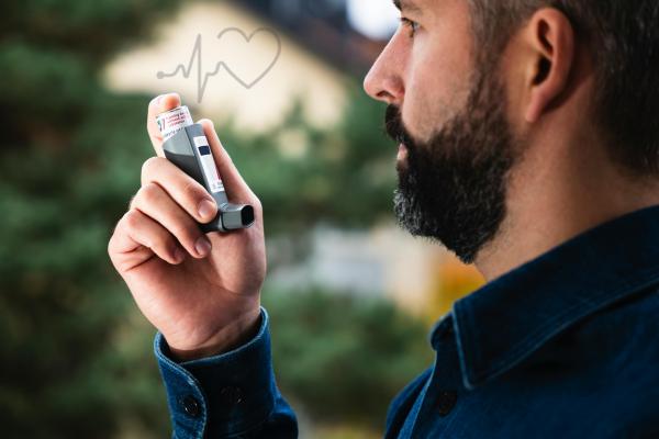 A man holding an asthma inhaler near his mouth, with a blurred outdoor background.