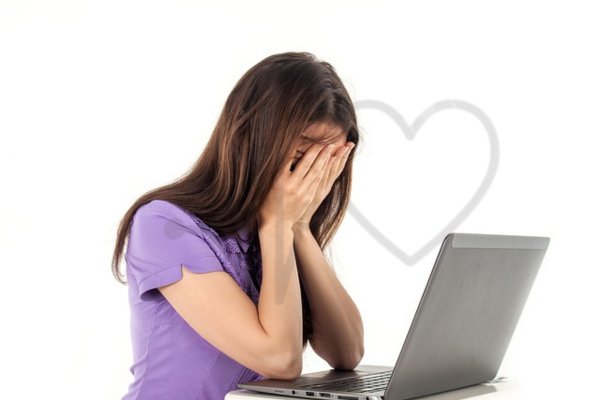 Woman sitting in front of a laptop with her face buried in hands, expressing stress or frustration.